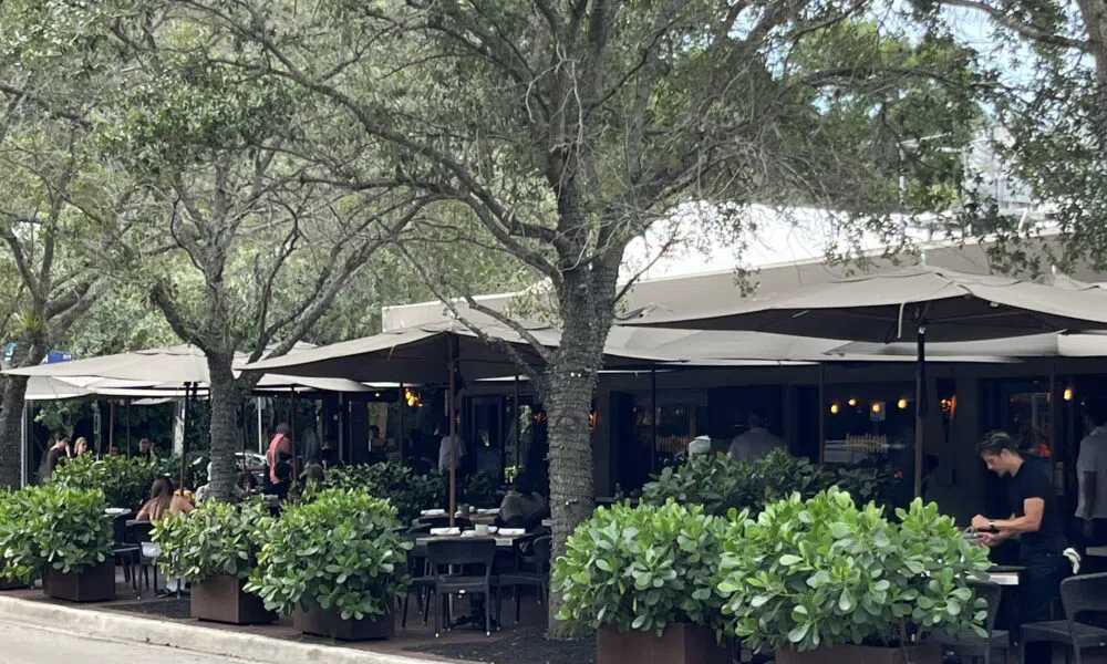 Commodore Plaza sidewalk cafe tables under tree canopy in Coconut Grove